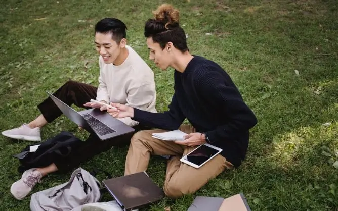 Hai sinh viên đang cùng tra cứu thông tin nên du học nước nào rẻ trên máy tính tại khuôn viên xanh